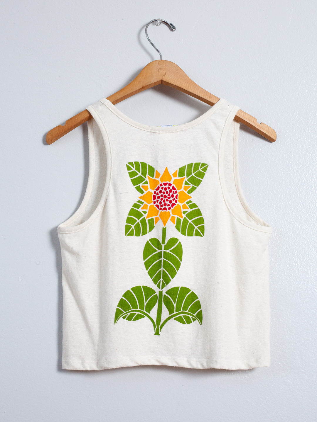White tank top with a colorful floral design on a wooden hanger against a light gray background