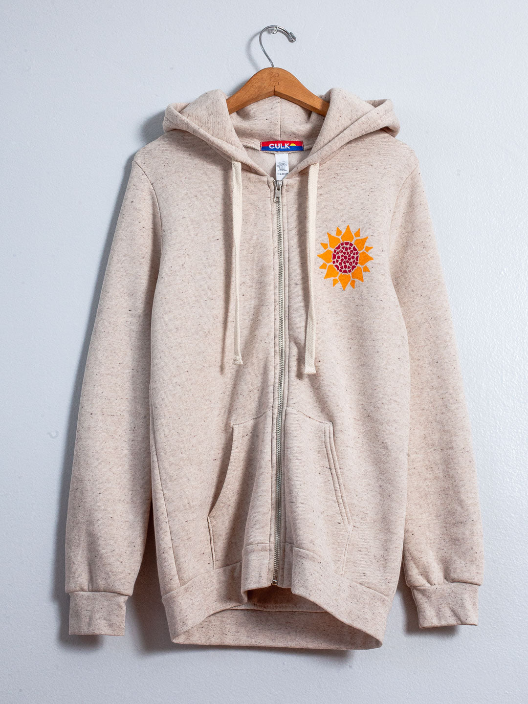 Beige hoodie with a sunflower design on a hanger against a light gray background