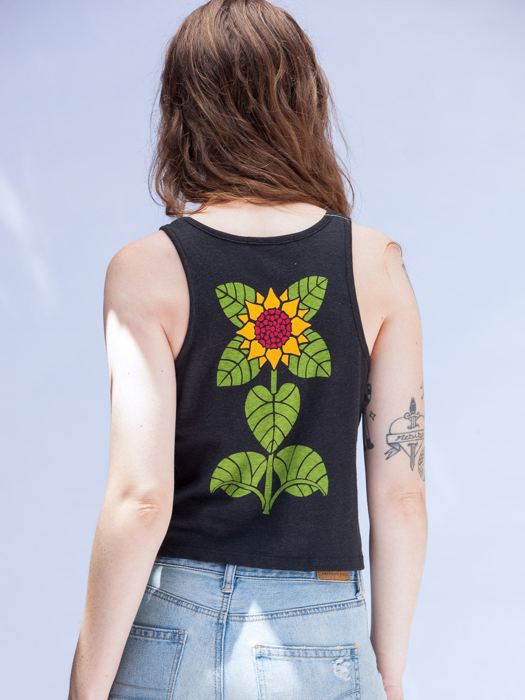 Person wearing a black tank top with a colorful floral design on the back against a light blue background