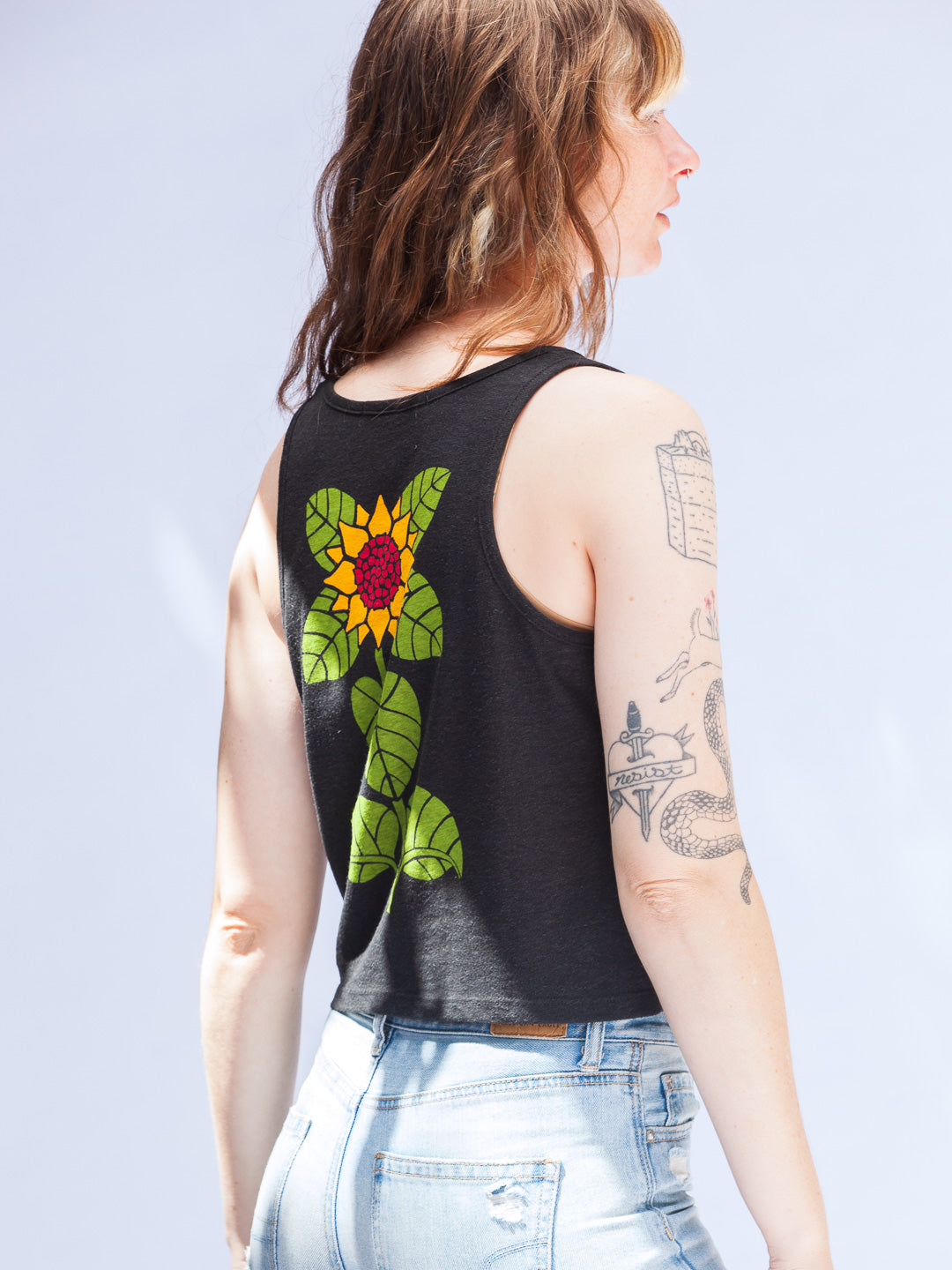 Person wearing a black sleeveless shirt with a colorful flower design on the back against a light gray background