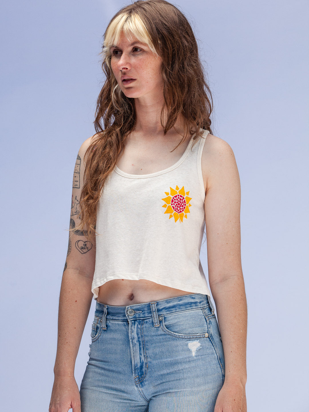 Woman wearing a white tank top with a sunflower design on a light blue background