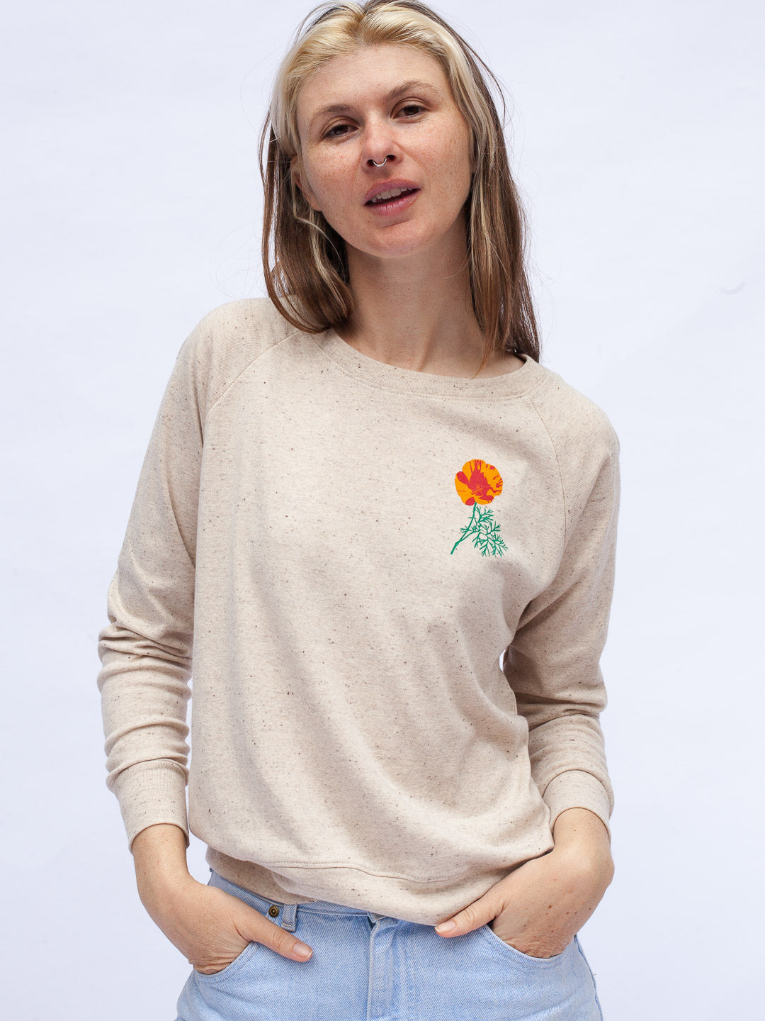 Woman wearing a beige sweater with a flower design on a light gray background