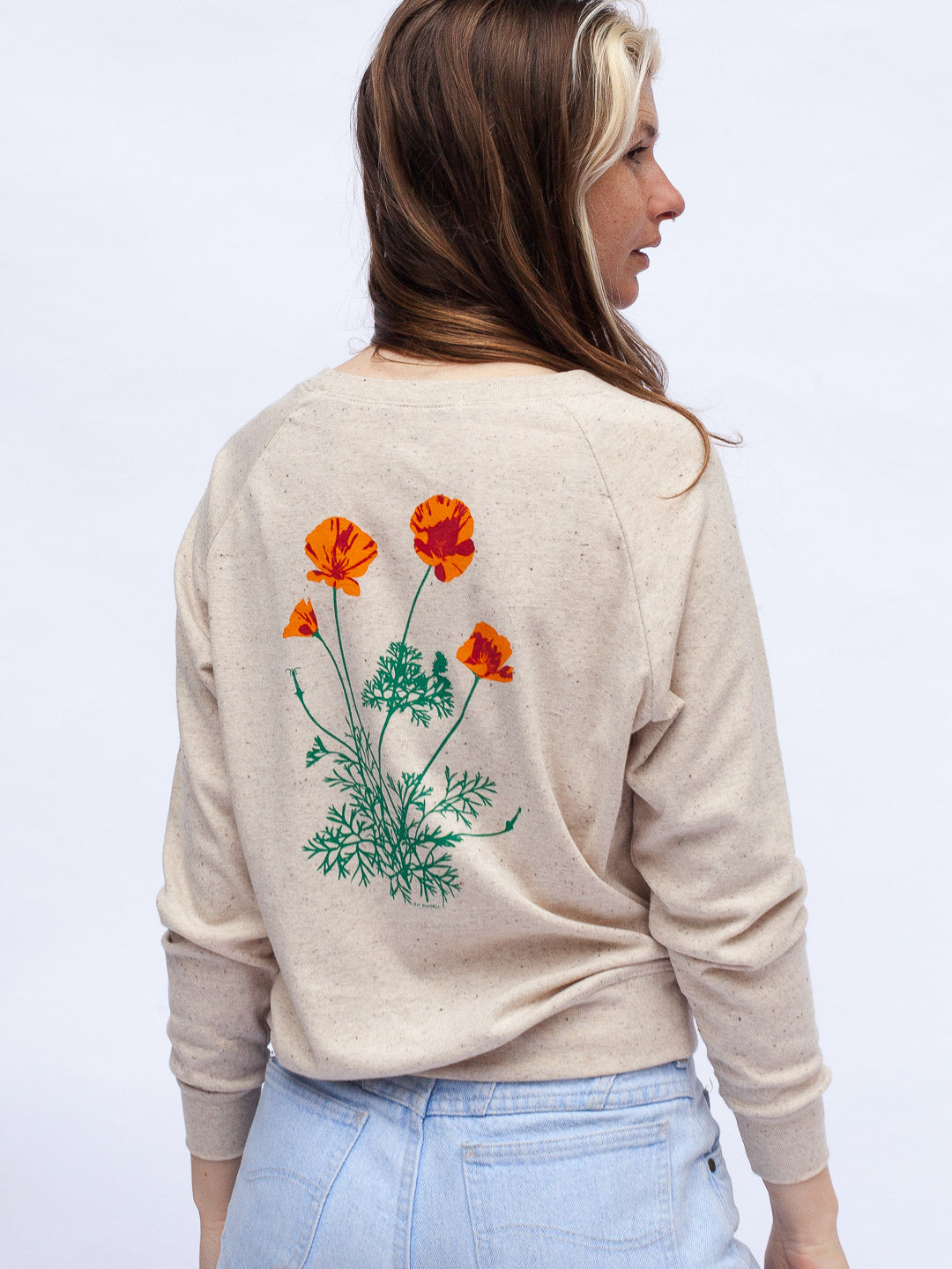 Woman wearing a beige sweater with a flower design on a light gray background