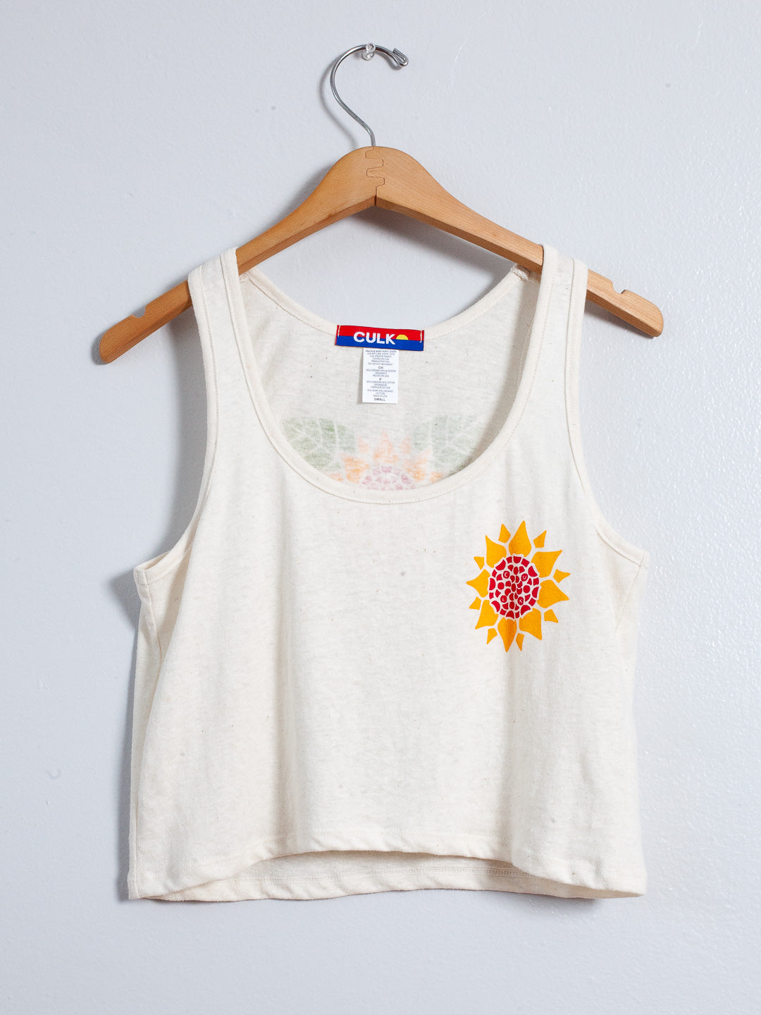 White tank top with a sunflower design on a hanger against a light gray background