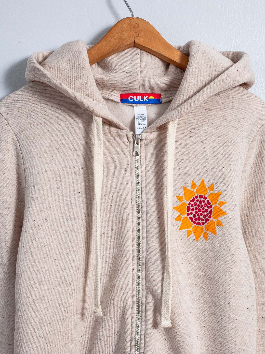 Beige hoodie with a sunflower design and CULK branding on a hanger.
